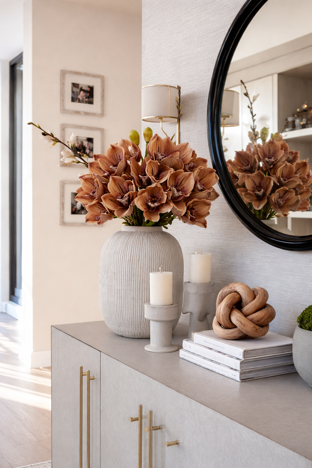 Decorative setup with a vase of flowers, candles, and books on a cabinet.