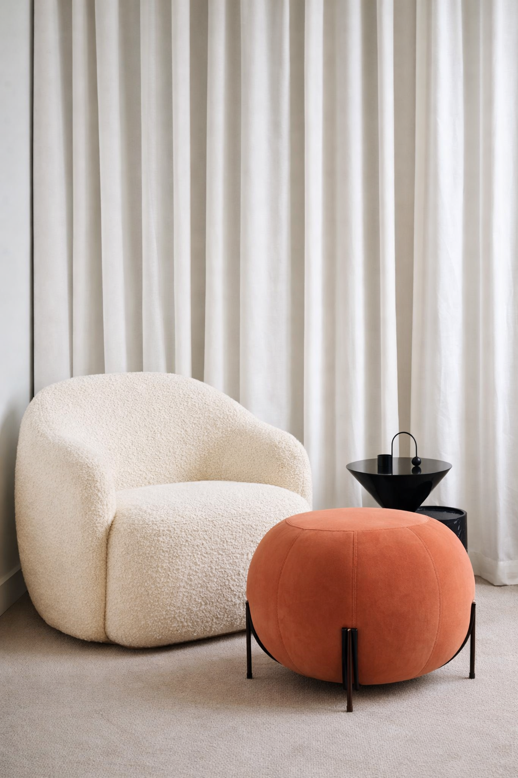 White armchair and orange ottoman in a room with white curtains.