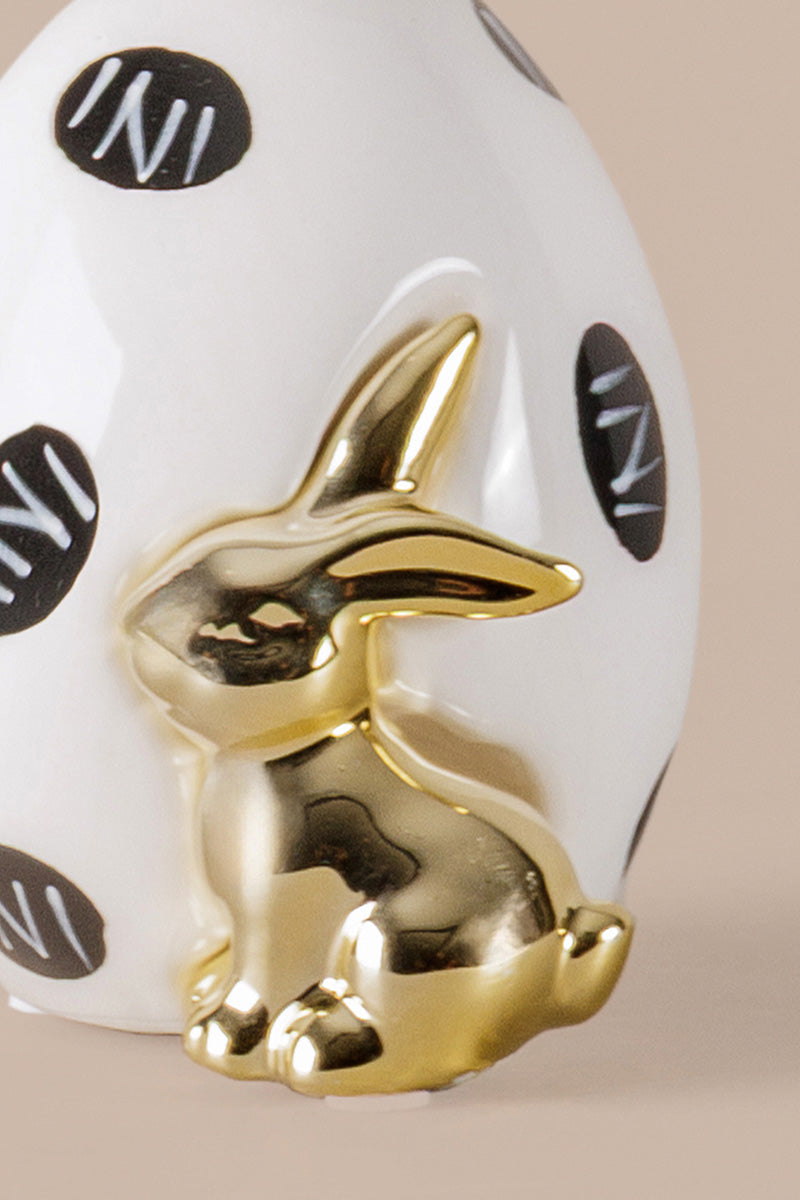 Decorative ceramic egg showing black dotted detailing and gold rabbit figure