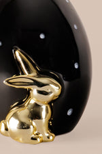 Decorative ceramic egg showing white polka dots and gold bunny detailing