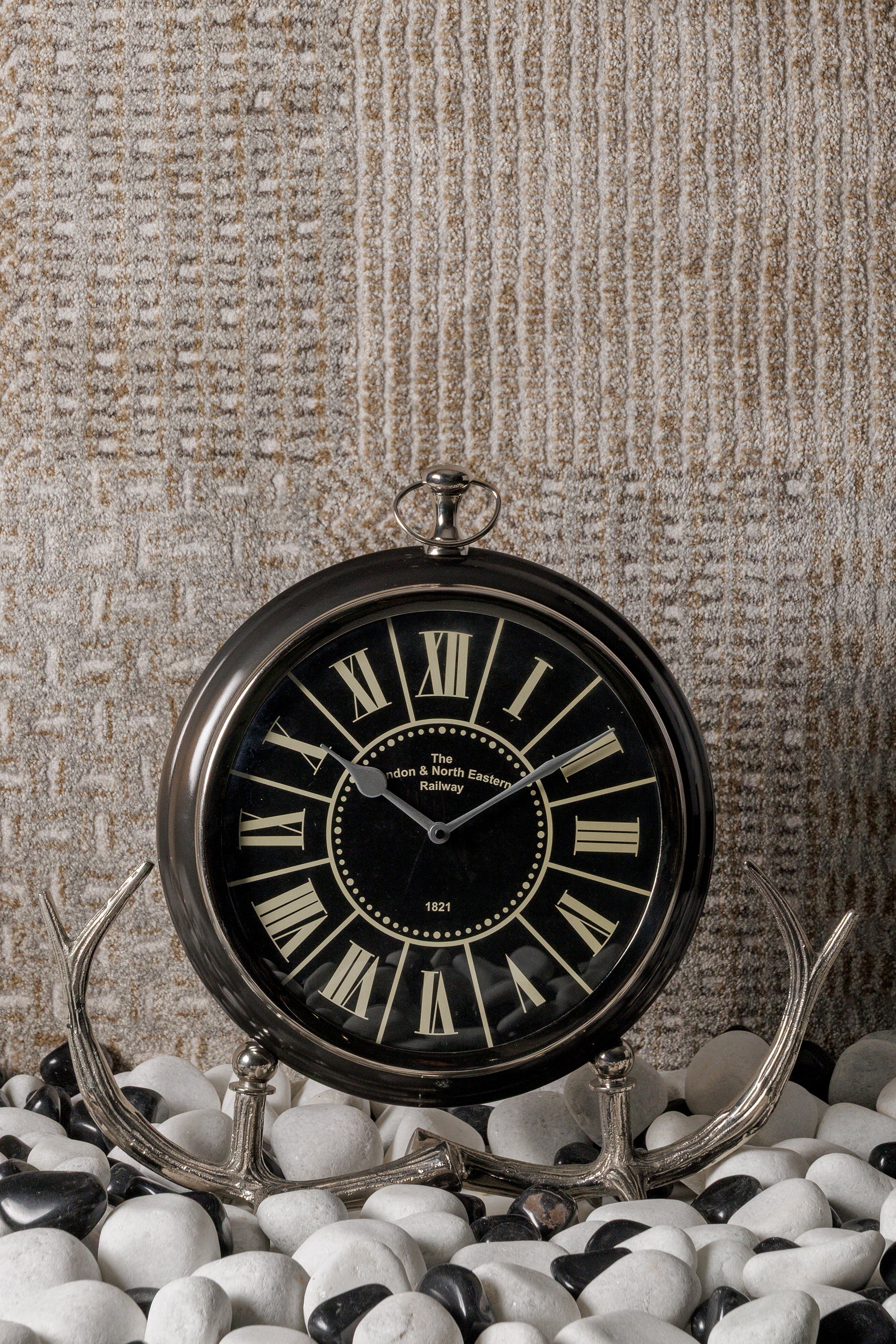 Decorative clock with black face and silver frame on a textured surface