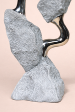 Abstract sculpture with stone-like gray elements and metallic accents on a beige background