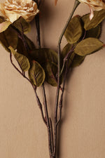 Artificial flower branch with leaves and a beige rose on a beige background