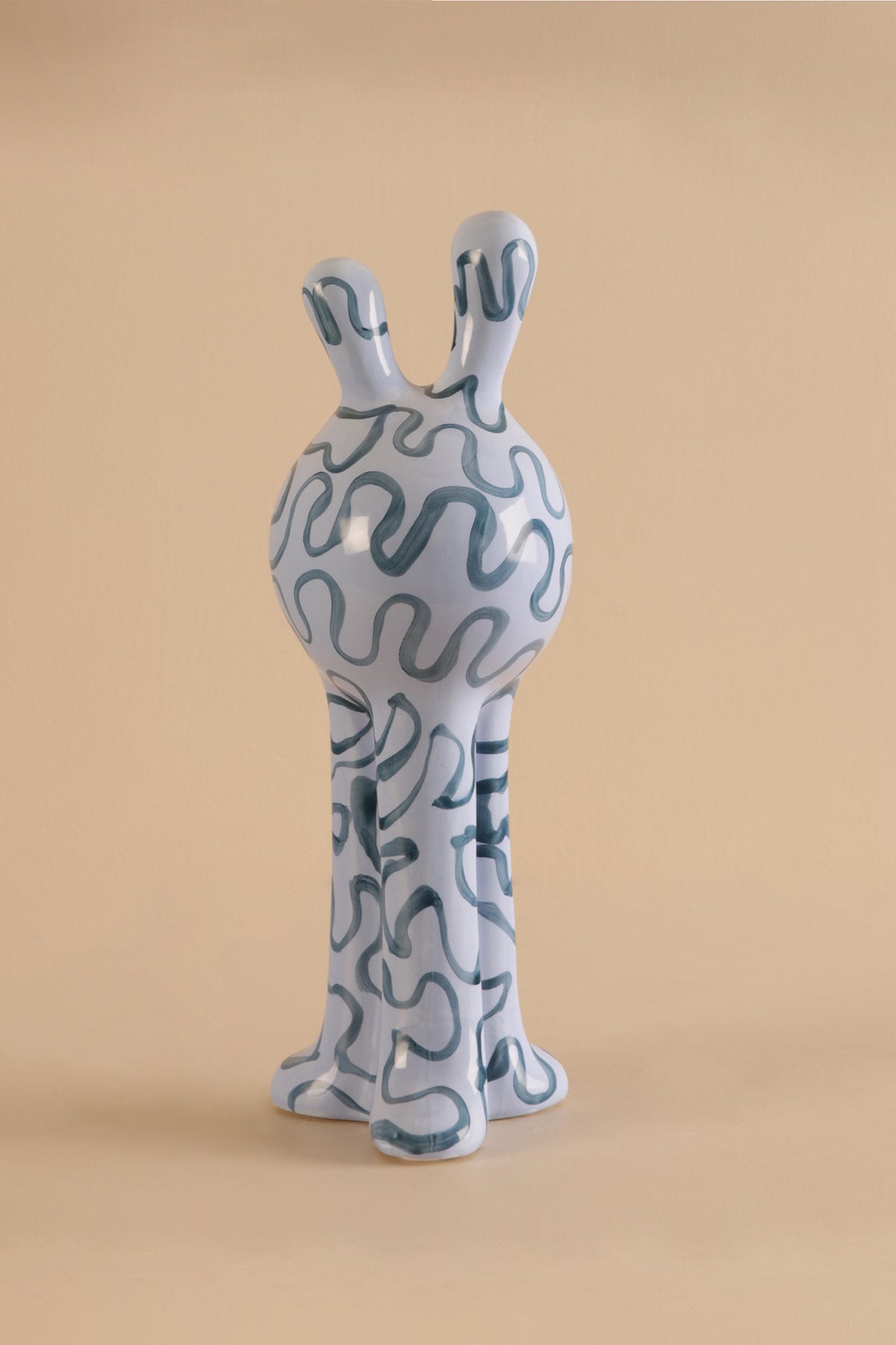 Ceramic sculpture of a creature with wavy patterns on a beige background