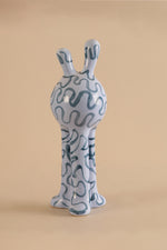 Ceramic sculpture of a creature with wavy patterns on a beige background