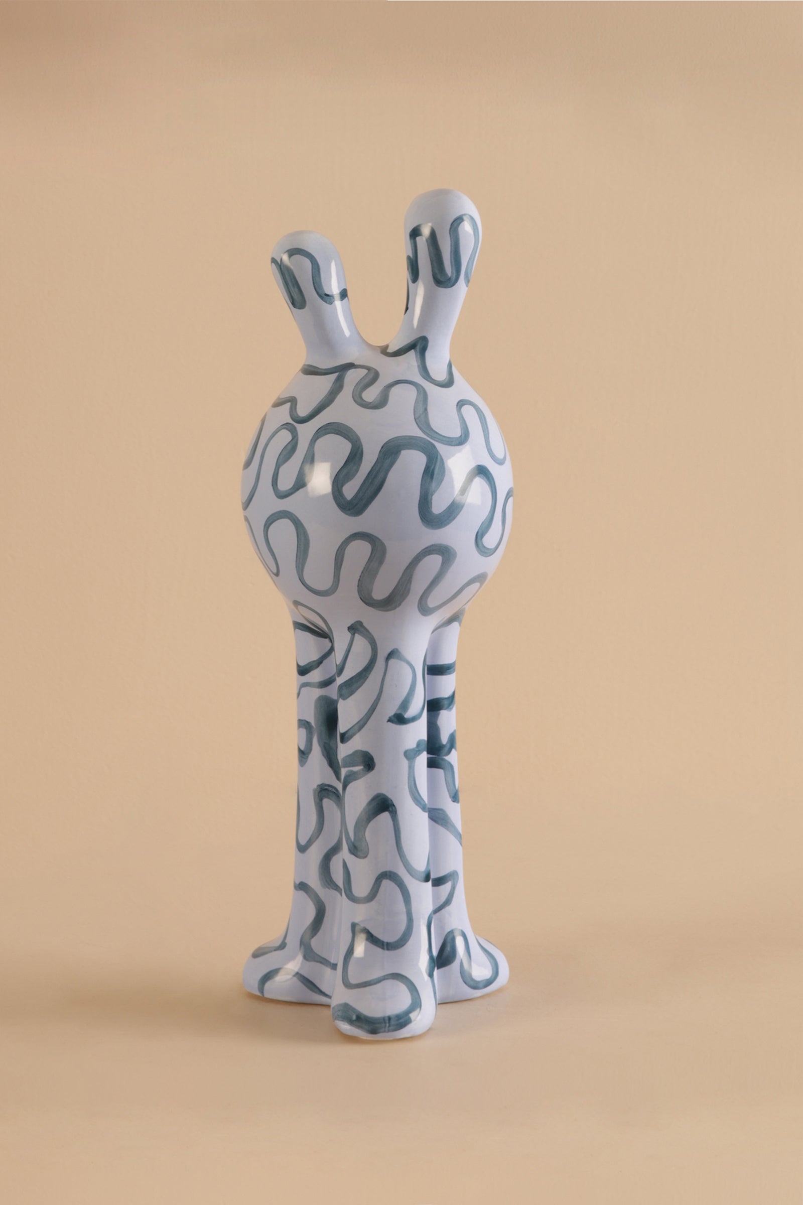 Ceramic sculpture of a creature with wavy patterns on a beige background