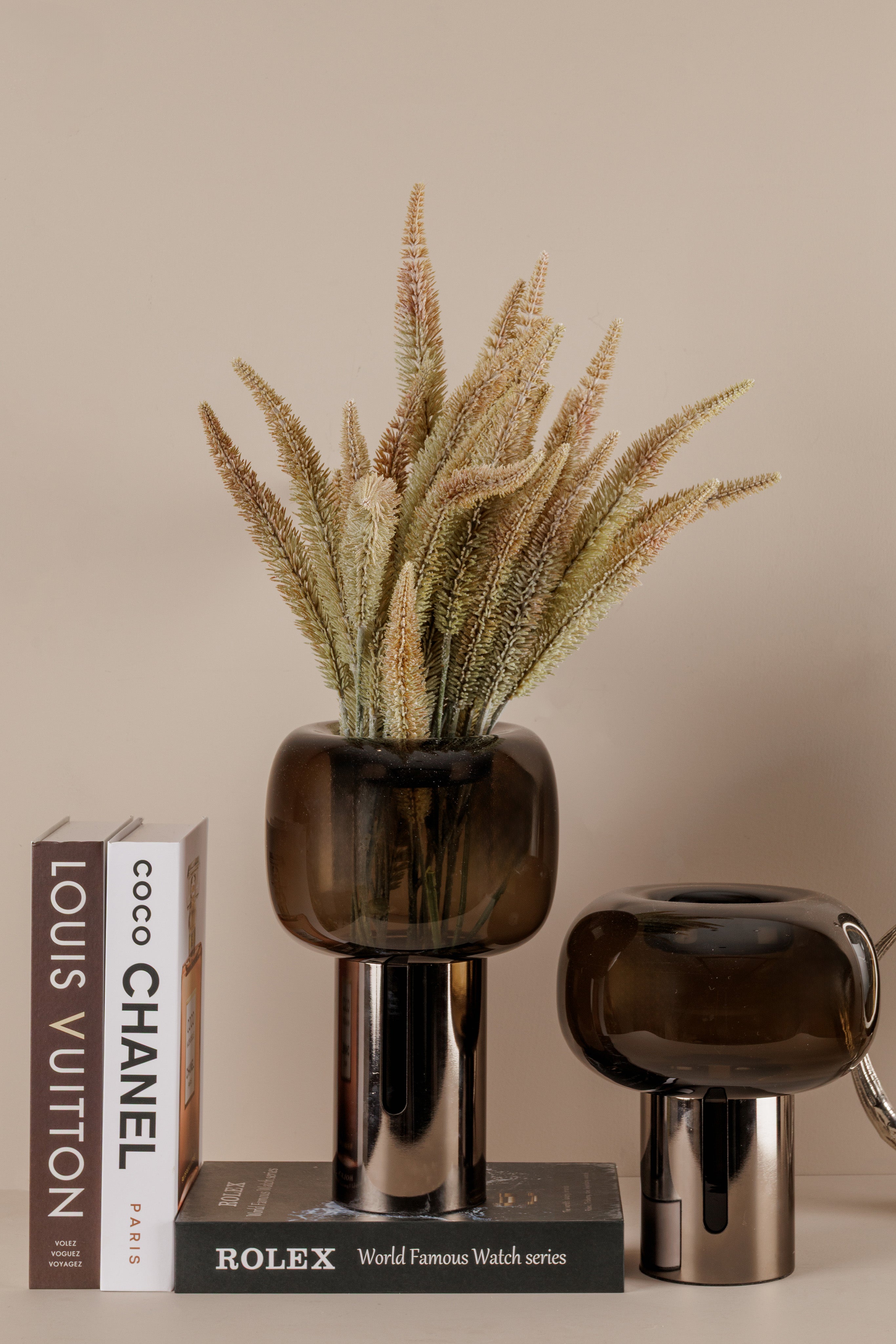 Decorative vases with a plant and luxury brand books on a beige background