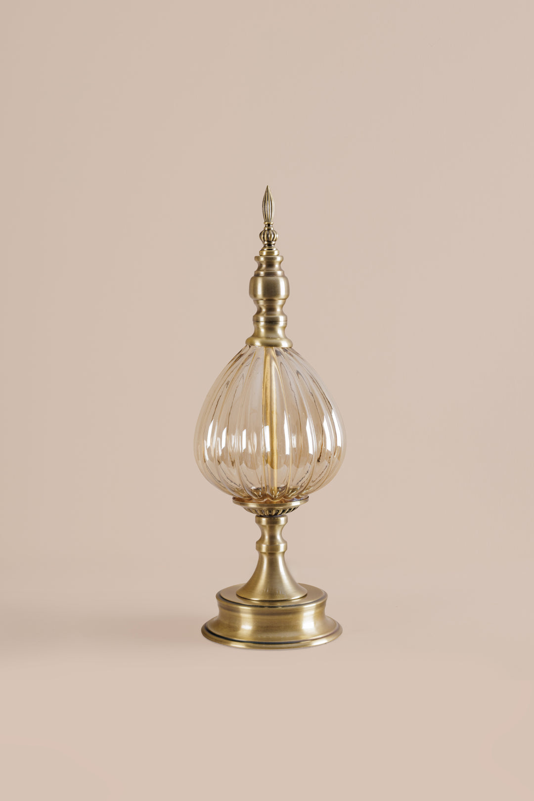 Decorative lamp with brass base and clear glass shade on a beige background
