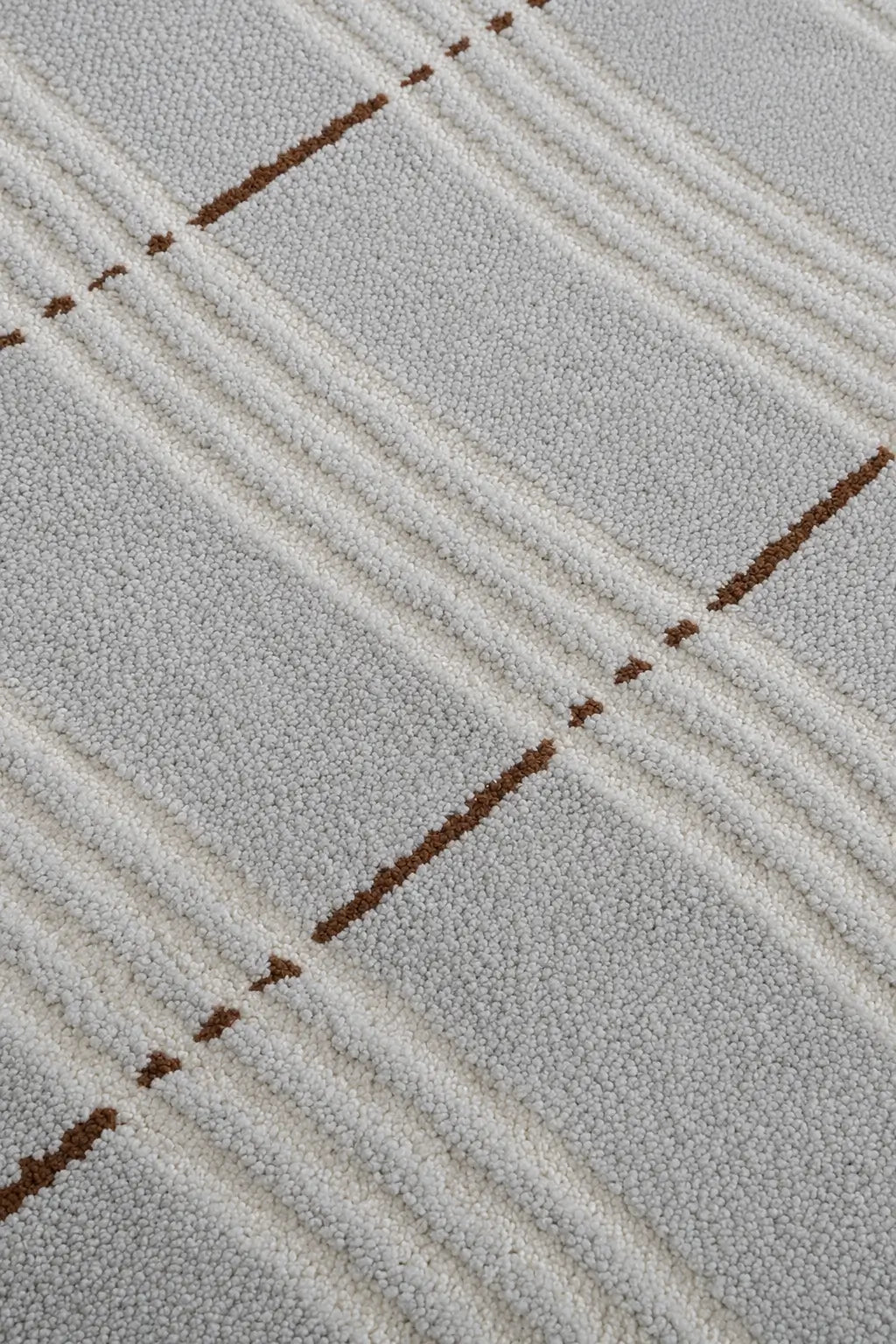 Close-up of a textured area rug with a modern plaid pattern in cream, light gray, and brown.