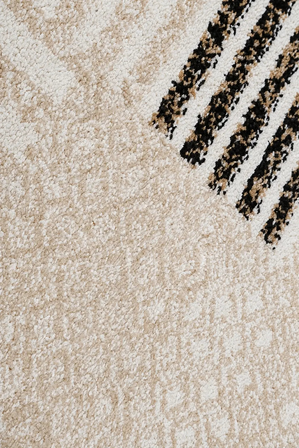 Close-up of a textured area rug in cream and beige with a pattern of black and beige diagonal stripes in the upper right corner.
