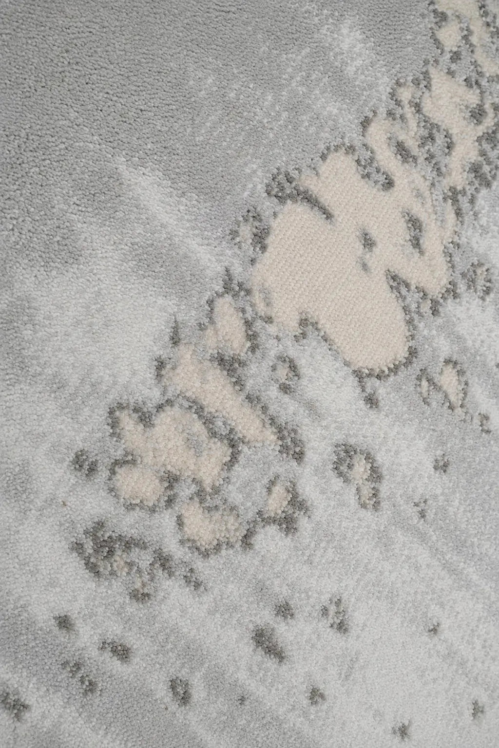 A close-up of a textured area rug featuring a modern abstract pattern in shades of light gray, beige, and white.
