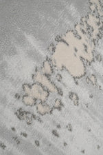 A close-up of a textured area rug featuring a modern abstract pattern in shades of light gray, beige, and white.