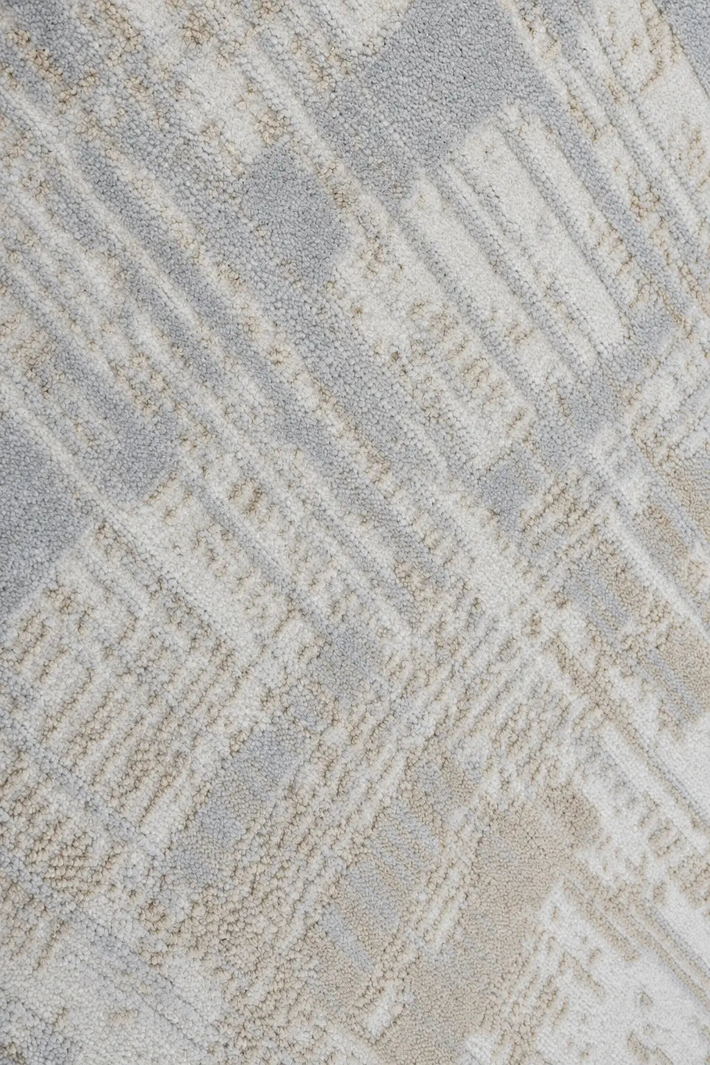 A close-up of a textured area rug featuring a modern geometric pattern in shades of light gray, beige, and off-white.