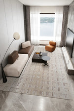 A modern living room featuring a large patterned area rug in beige and gray, styled with a cream and brown sectional sofa, a dark wood coffee table, a black floor lamp, and a large window overlooking a body of water.