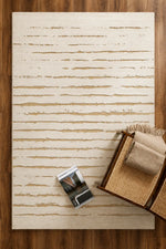 A rectangular area rug with a distressed horizontal stripe pattern in cream and tan, styled on a dark wood floor with a woven basket and a magazine nearby.