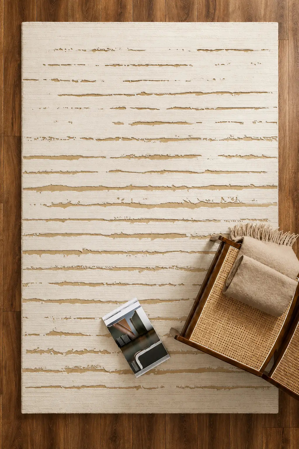 A rectangular area rug with a distressed horizontal stripe pattern in cream and tan, styled on a dark wood floor with a woven basket and a magazine nearby.