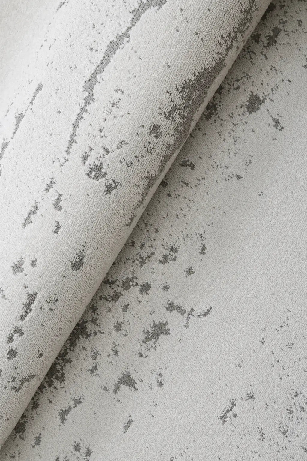 A close-up of a textured fabric or wallpaper sample in off-white with a distressed gray mottled pattern, shown folded diagonally.
