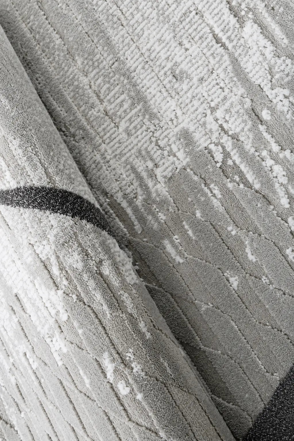 Close-up of a textured area rug in light gray and white with a dark charcoal curved stripe detail.