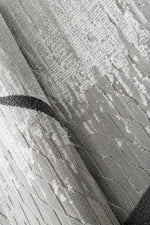 Close-up of a textured area rug in light gray and white with a dark charcoal curved stripe detail.