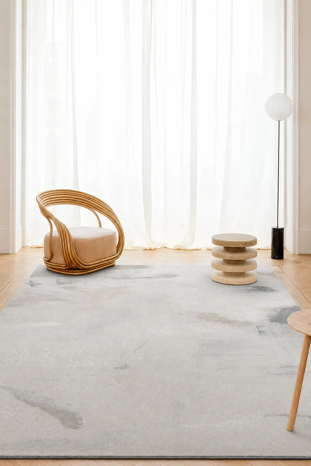 A large light gray and white abstract patterned area rug in a bright, modern room with a wicker chair, a small wooden side table, and a floor lamp.