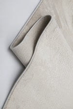 A close-up of a light beige textured rug with a rolled corner showing its loop height and woven texture, set against a clean white background.