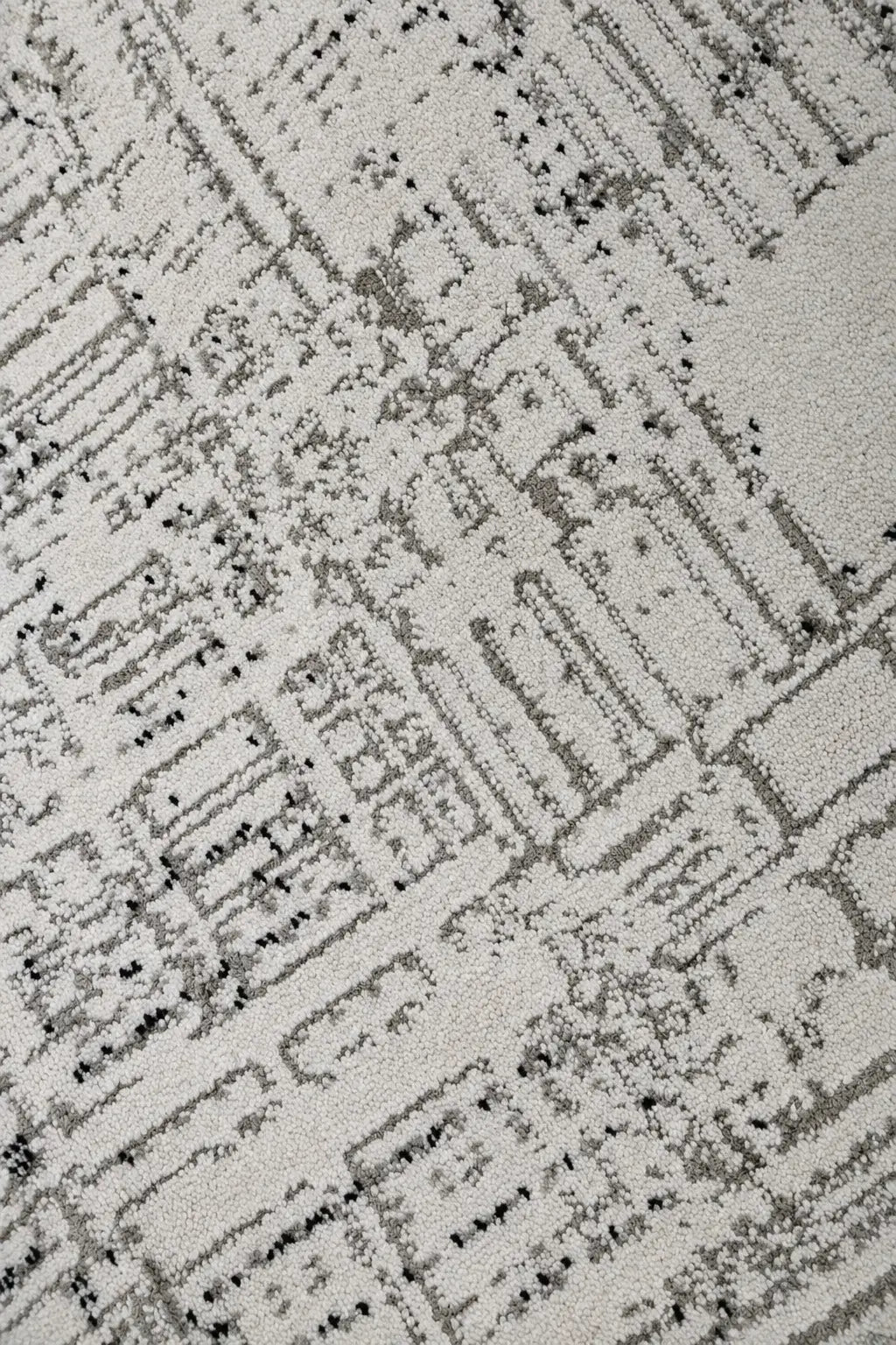 A close-up of a textured area rug featuring an abstract, distressed city-block pattern in shades of gray and black on a warm off-white background.