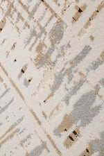A close-up of a textured area rug featuring an abstract, distressed pattern in beige, gray, and off-white.