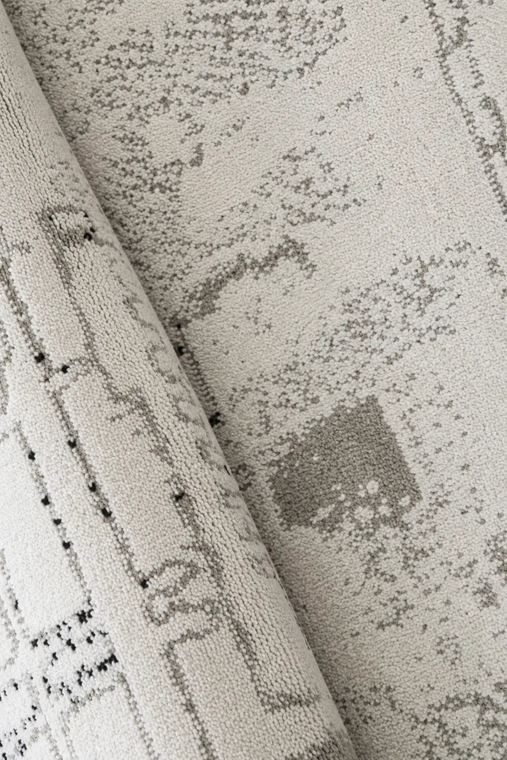 Close-up of a textured area rug with a distressed, abstract pattern in shades of gray and black on a warm off-white background.