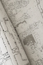Close-up of a textured area rug with a distressed, abstract pattern in shades of gray and black on a warm off-white background.