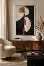 A large framed abstract wall art piece hangs above a wooden console in a styled living room. The artwork features bold black, cream, and tan geometric shapes.