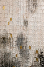A close-up of a textured surface featuring overlapping translucent scale-like shapes in soft beige, gray, and black tones, accented with scattered metallic gold shapes.