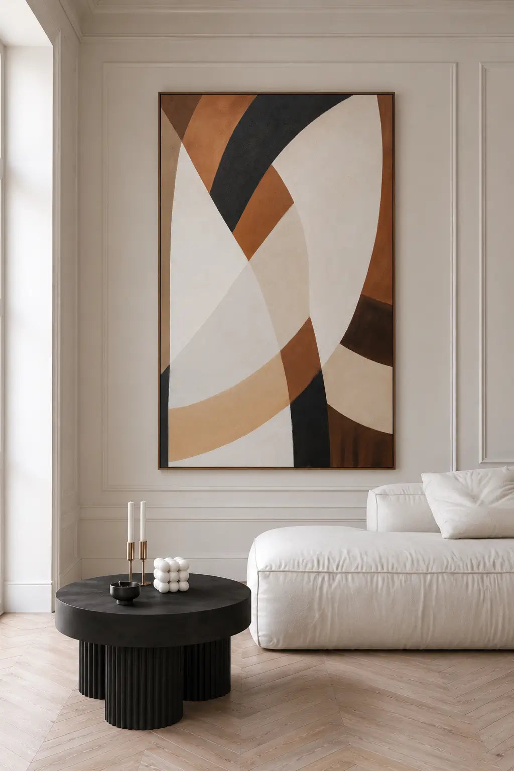 A large abstract wall art print with sweeping curved shapes in cream, tan, brown, black, and beige, displayed in a modern living room above a white sofa and a black round coffee table.