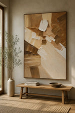 Large framed abstract wall art in warm beige, brown, cream, and white tones, displayed above a wooden bench in a softly styled interior with a vase and rug.
