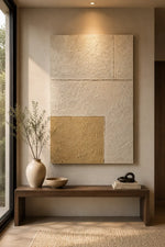 Large textured wall art made of three rectangular panels in warm off-white and beige tones, with one lower-left panel in mustard gold, displayed above a wooden bench in a minimalist interior setting.