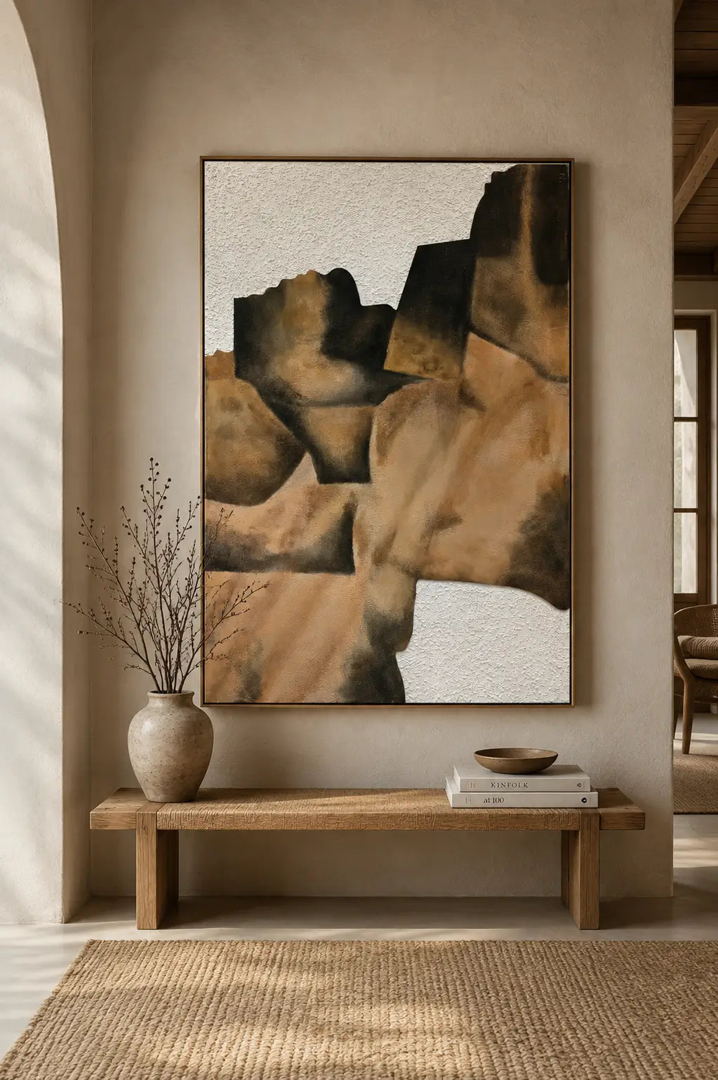 A framed abstract wall art print with geometric shapes in tan, brown, black, and off-white, displayed above a wooden bench in a warm neutral interior setting.