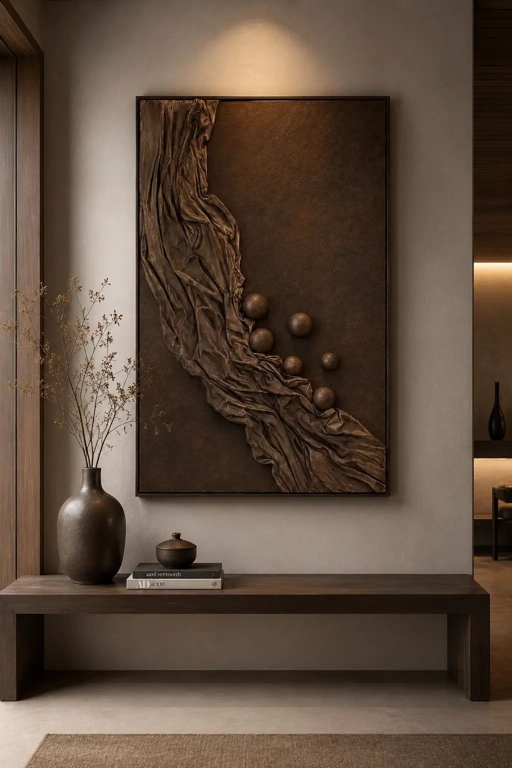 A large vertical wall art piece with a textured bronze and brown abstract design, displayed in a modern, minimalist interior setting above a dark wooden console table.
