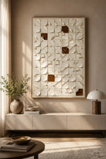 Large framed abstract wall art with a geometric 3D textured pattern in cream and brown, displayed in a modern living room setting above a console table.
