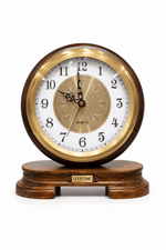 A round quartz clock with a dark brown wood-grain outer frame, a polished gold-tone bezel, and a white dial with black numerals. It sits on a matching dark brown wooden base with a small gold plaque that reads 'GOOD TIME'.