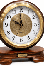 A round wooden desk clock with a polished gold-tone bezel, white dial, black numerals and hands, and a decorative gold medallion in the center. The clock sits on a dark wood base with a small gold plaque that reads 'GOOD TIME'.