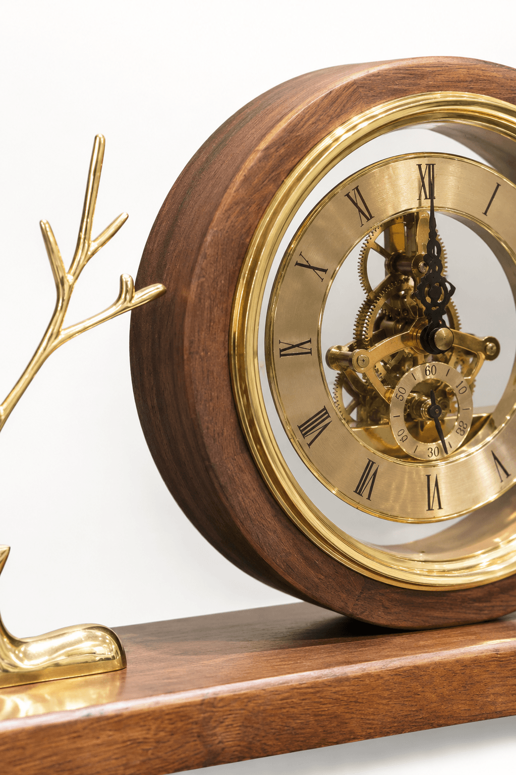 Close-up of a decorative mantel clock with a polished wooden body, gold-tone brass frame, Roman numerals, visible internal gears, and a matching wooden base with a gold branch-like ornament on the left.