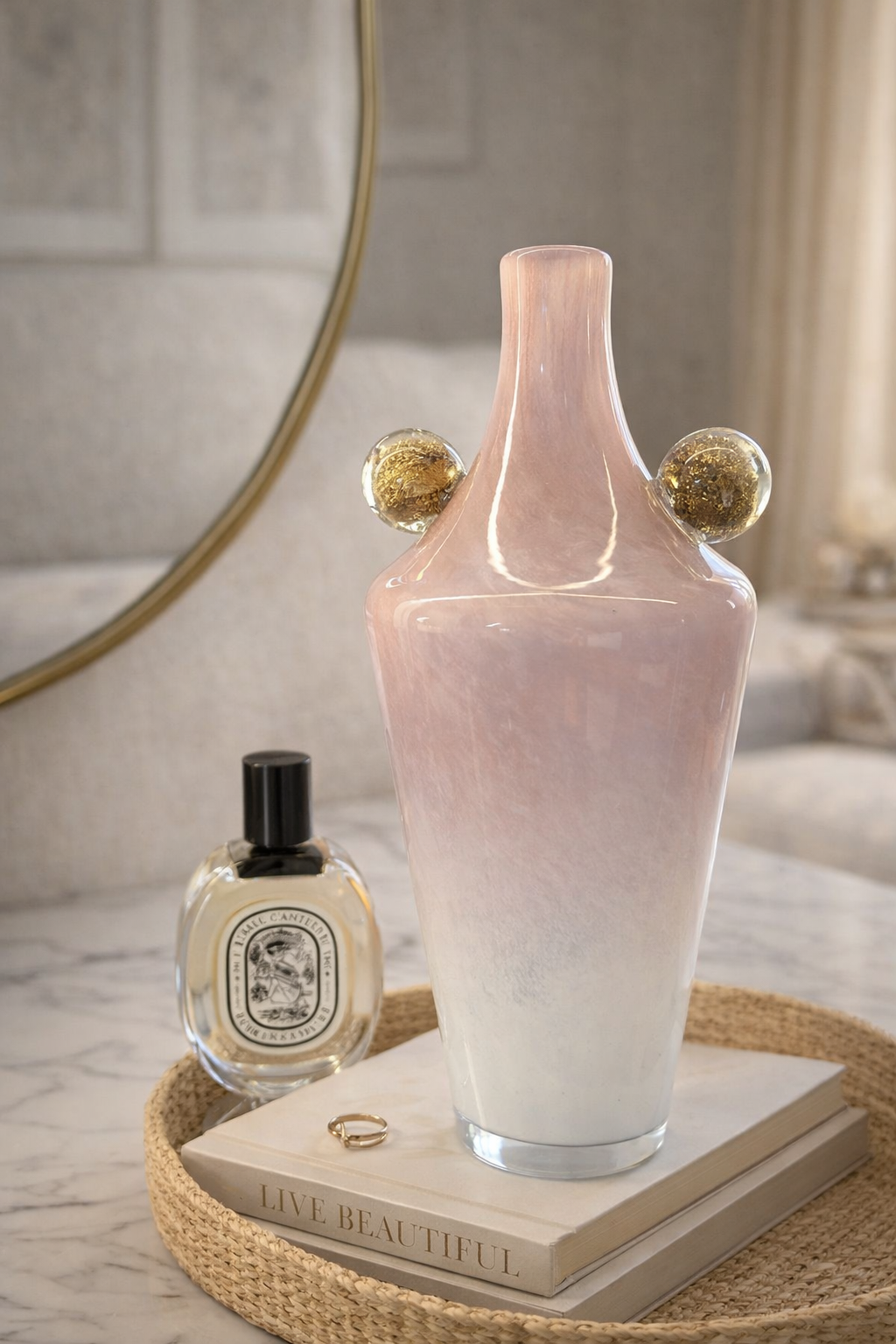 Pink vase with gold accents on a tray with a book and perfume bottle.