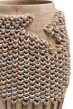 Close-up of a textured ceramic vase with a woven, chainmail-like pattern in earthy beige and gray tones on a white background.