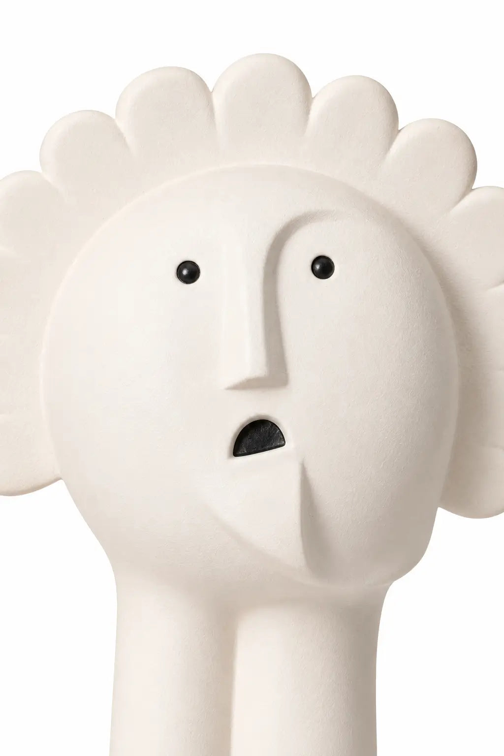 A close-up of a sculptural white ceramic figurine with a stylized face, black eyes, and a small black mouth, set against a plain white background.