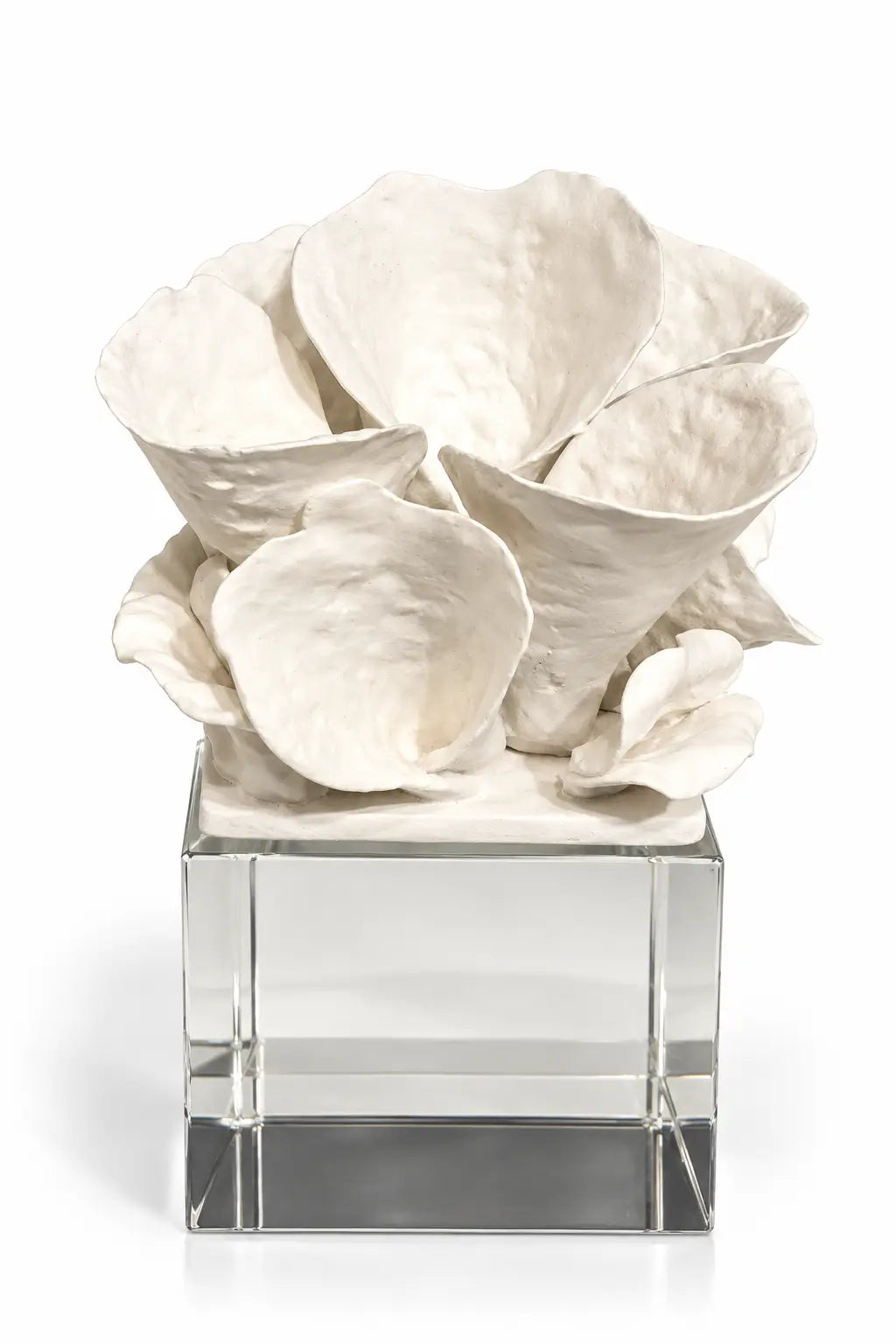 An off-white sculptural floral arrangement with textured, petal-like forms displayed on a clear glass cube pedestal against a white background.