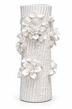 A white textured ceramic vase decorated with large white artificial flowers and green leaves, shown against a plain white background.
