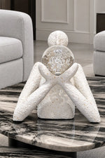 A decorative white textured figurine with a clear glass sphere head containing a snowflake design, displayed on a black and white marble coffee table in a modern living room setting.