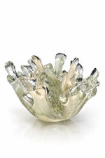 A sculptural, hand-blown glass bowl with a flared, coral-like rim, featuring a translucent iridescent finish with green, gold, and gray tones, set against a plain white background.