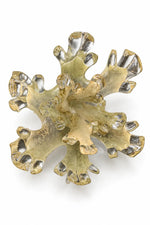 A sculptural, organic-shaped brooch or decorative piece made of layered translucent and metallic gold-toned material, photographed on a clean white background.