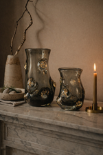 Two glass vases with decorative elements on a marble surface with a candle in the background.