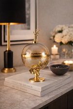 Decorative gold and glass sphere on books with a lamp and candles in the background